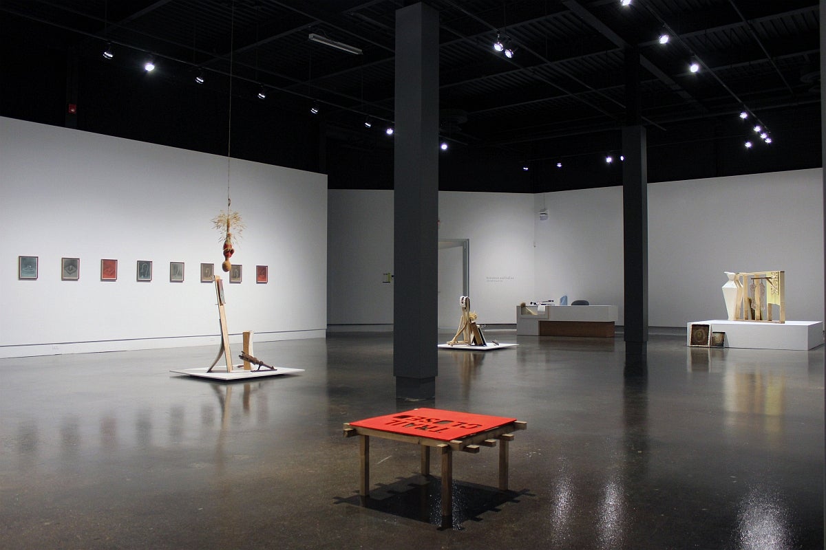 View of an art gallery installation with several assemblages on the floor and a low red table topped with a "Trail closed" sign.