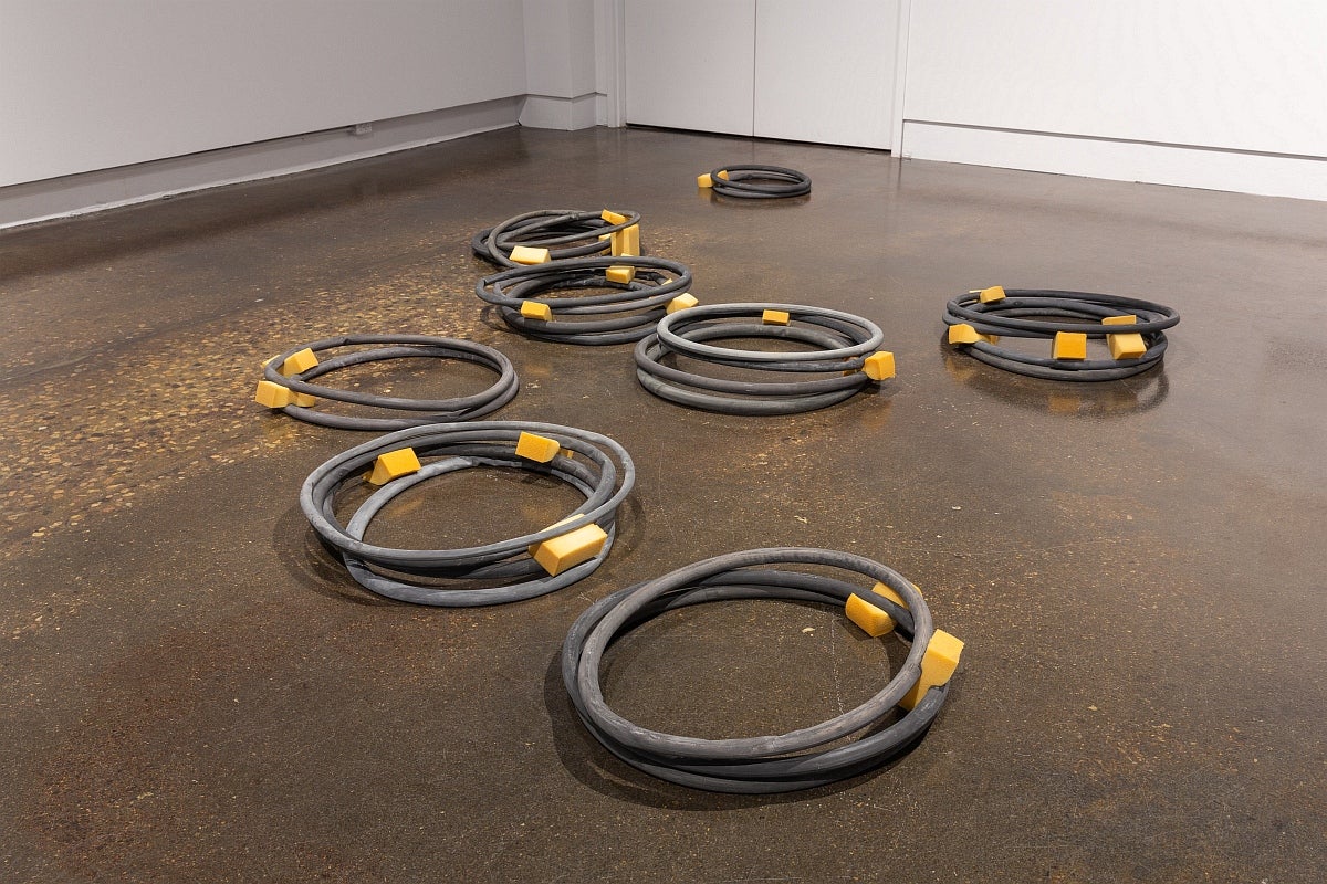 Artwork on gallery floor. Circular black plaster sculptures stacked in 8 groups, with yellow upholstery foam between layers. 