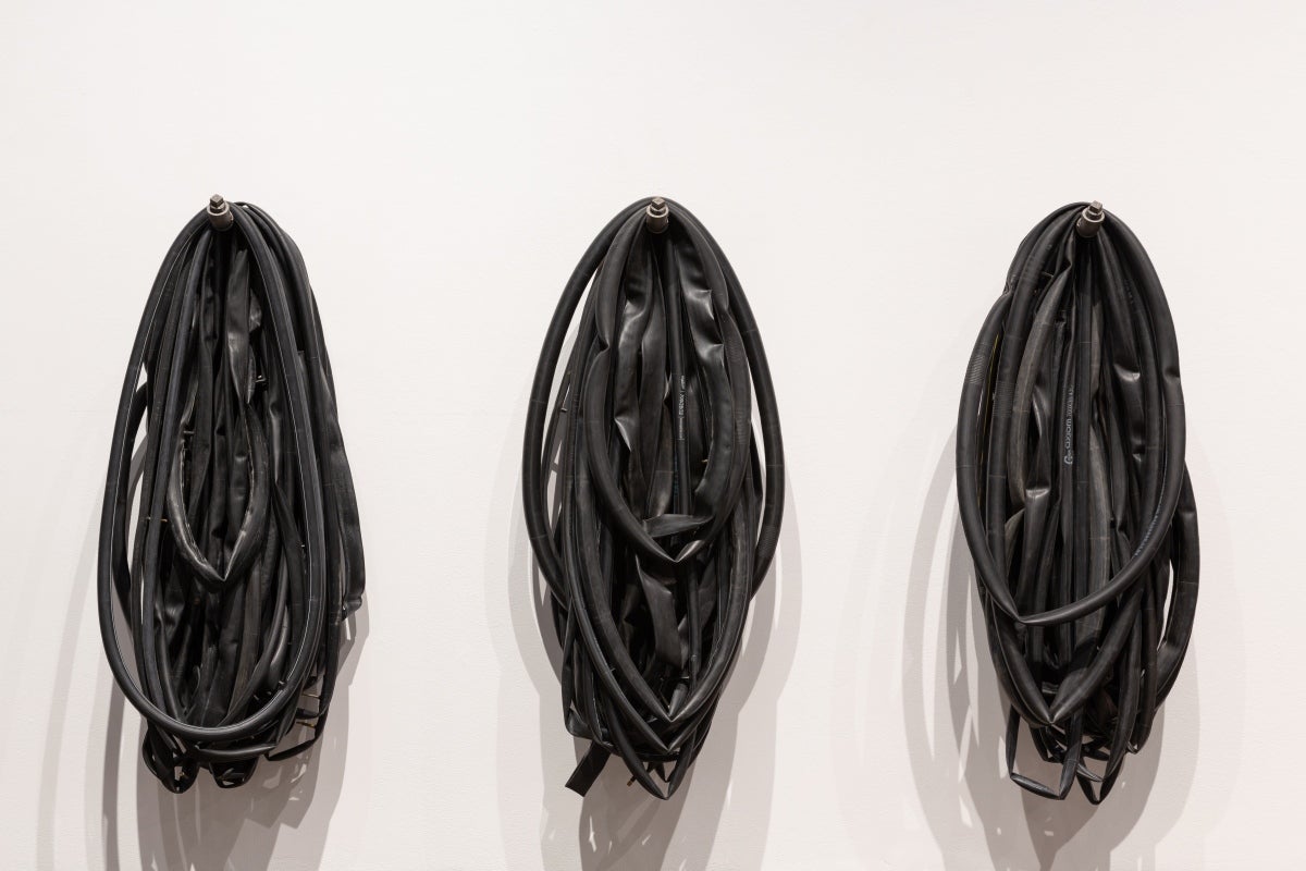 Detail of 3 sculptures of multiple, deflated, bicycle tire tubes hanging from industrial steel brackets.