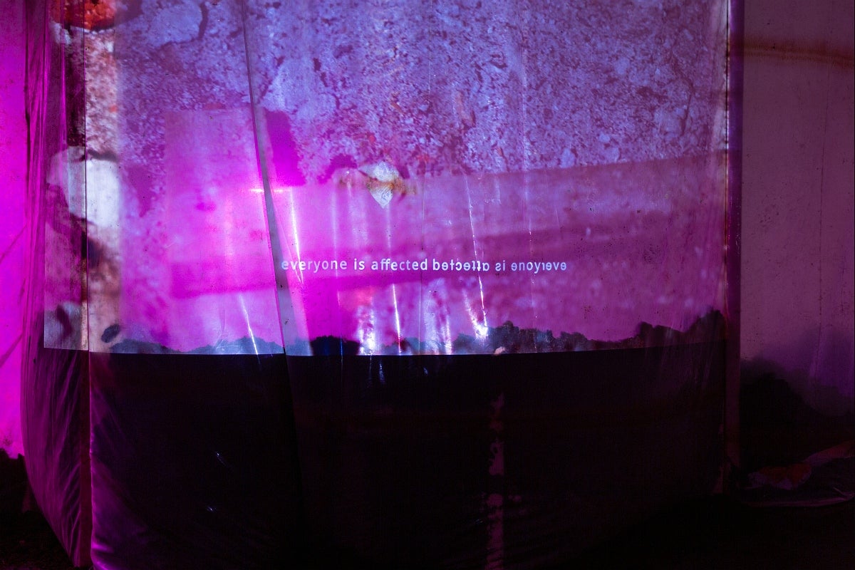 Installation in gallery. Magenta projection of abstracted image and the words "everyone is affected" shown readable and mirrored