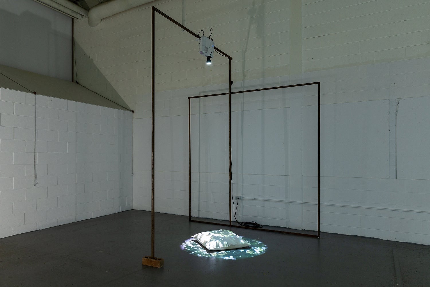 Industrial space with artwork. Metal frame supports a digital projector shining the image of dappled sunlight on a floor pillow