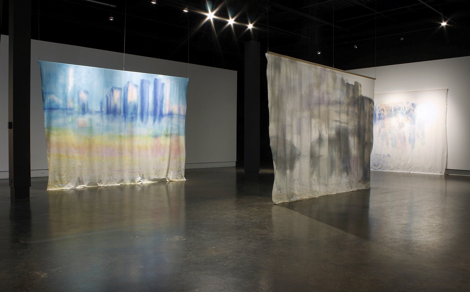 Art gallery with large rectangular hanging banners with ink wash paintings of cityscapes. 