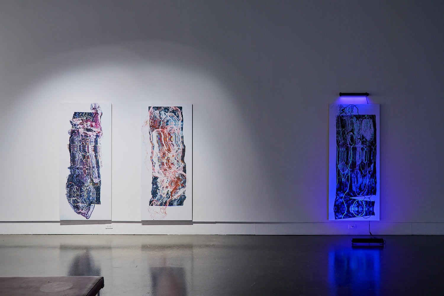 Art gallery installation of three large scale prints of distorted medical scans, one lit by ultraviolet light.