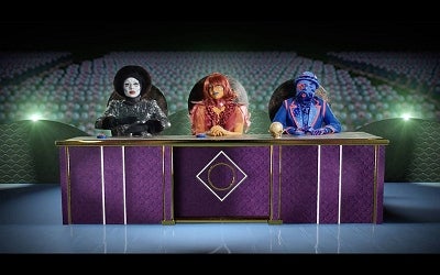 A panel of three elaborately dressed extraterrestrial judges sit behind a large podium inside of a large theatre