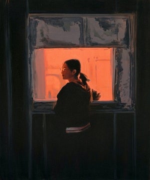 A woman with her hair in a ponytail and wearing glasses stands in a darkened room in front of a bright orange window and looks over her left shoulder