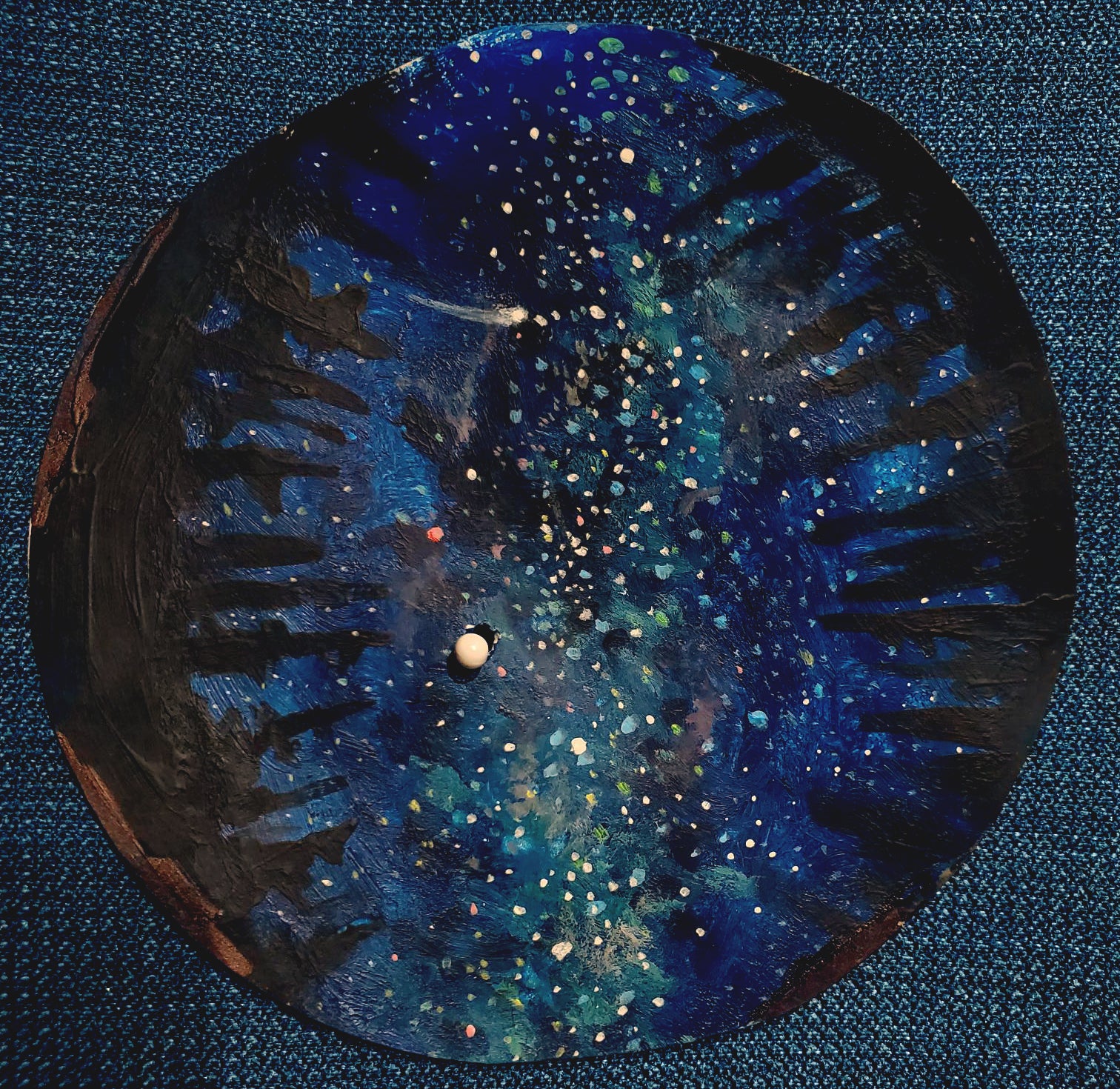 Circular painting of the night sky rimmed with dark evergreen trees.