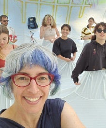Selfie of person with blue hair with six people behind, all with the same white fabric gathered around their waists.
