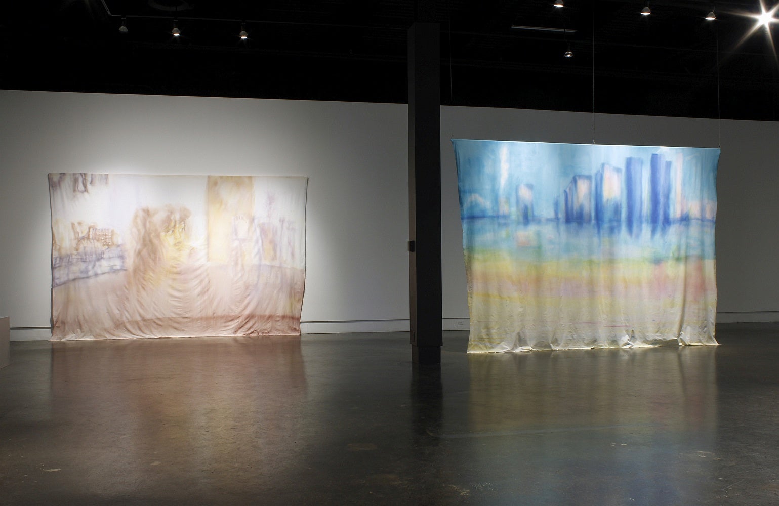 Art gallery with large rectangular hanging banners with ink wash paintings of a cityscape and a child's face. 