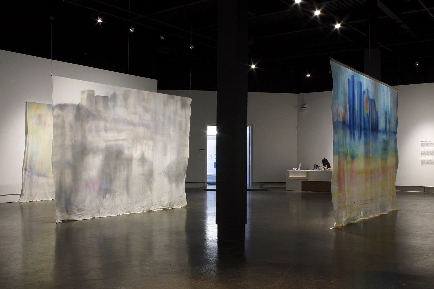 Art gallery with large rectangular hanging banners with ink wash paintings of cityscapes. 