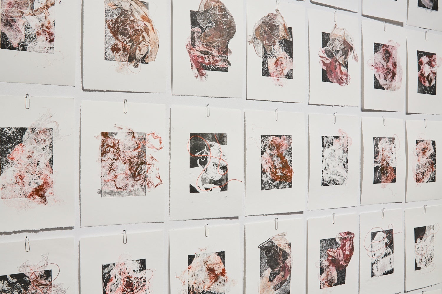 Detail of multiple prints depicting medical waste hung by paperclips in a grid pattern.