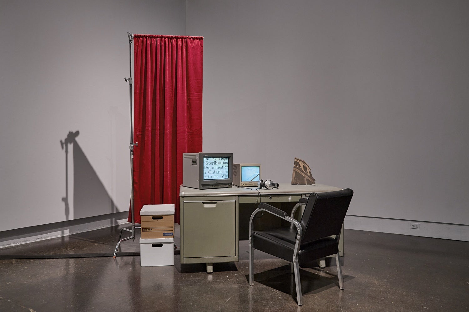 Videos run on two vintage televisions sitting on industrial office desk in front of  a privacy screen.