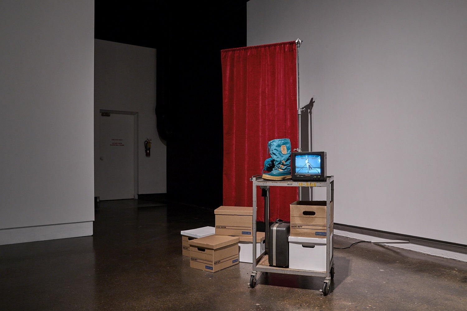 A metal cart with a small monitor, winter boots and bankers boxes, sits in front of a privacy curtain