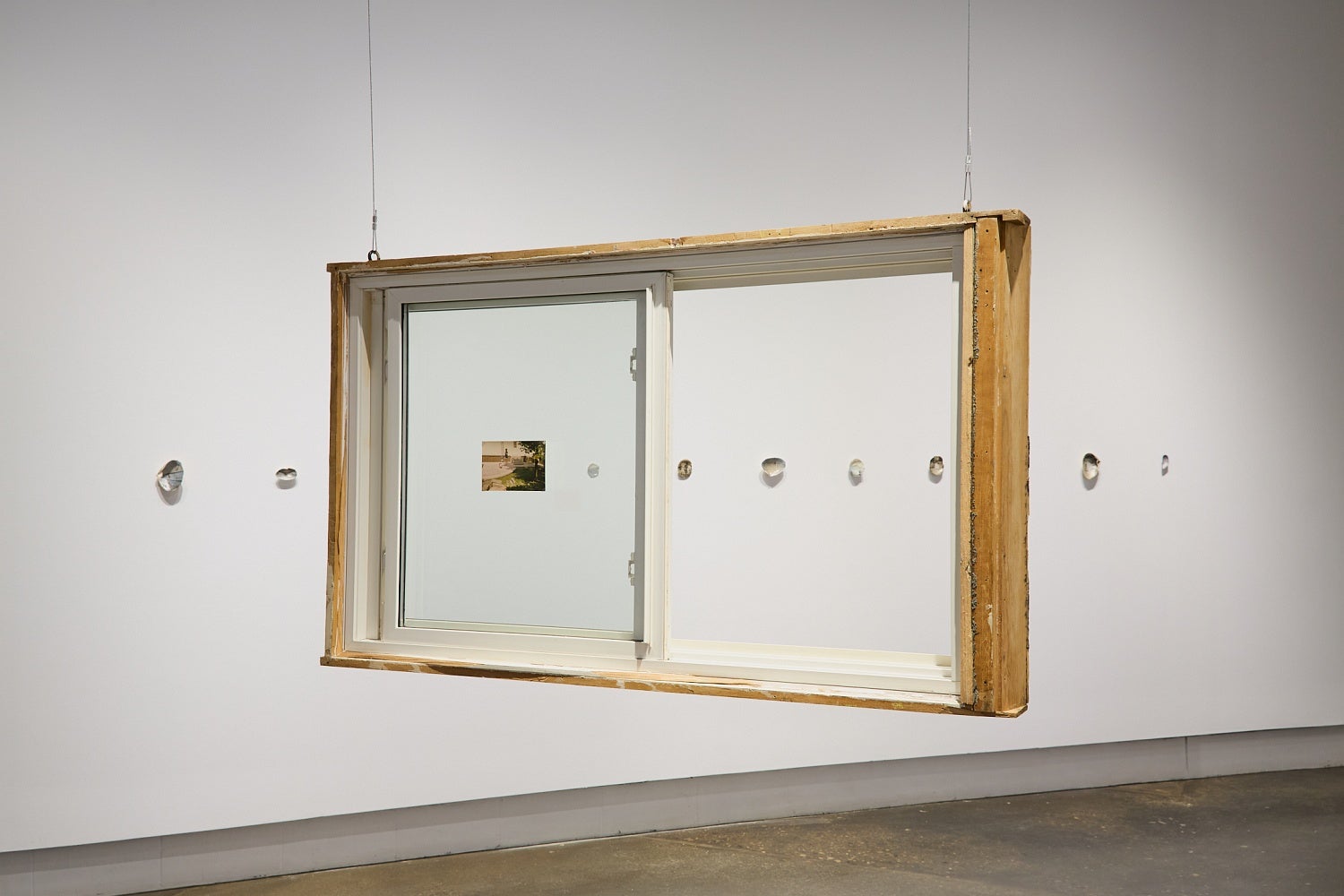 A salvaged house window hangs from the ceiling in front of a wall displaying a row of shells.