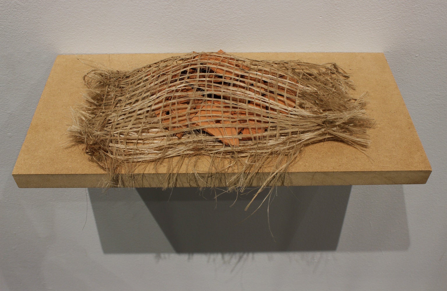 Multiple clay tiles are wrapped in woven jute are displayed on a shelf.