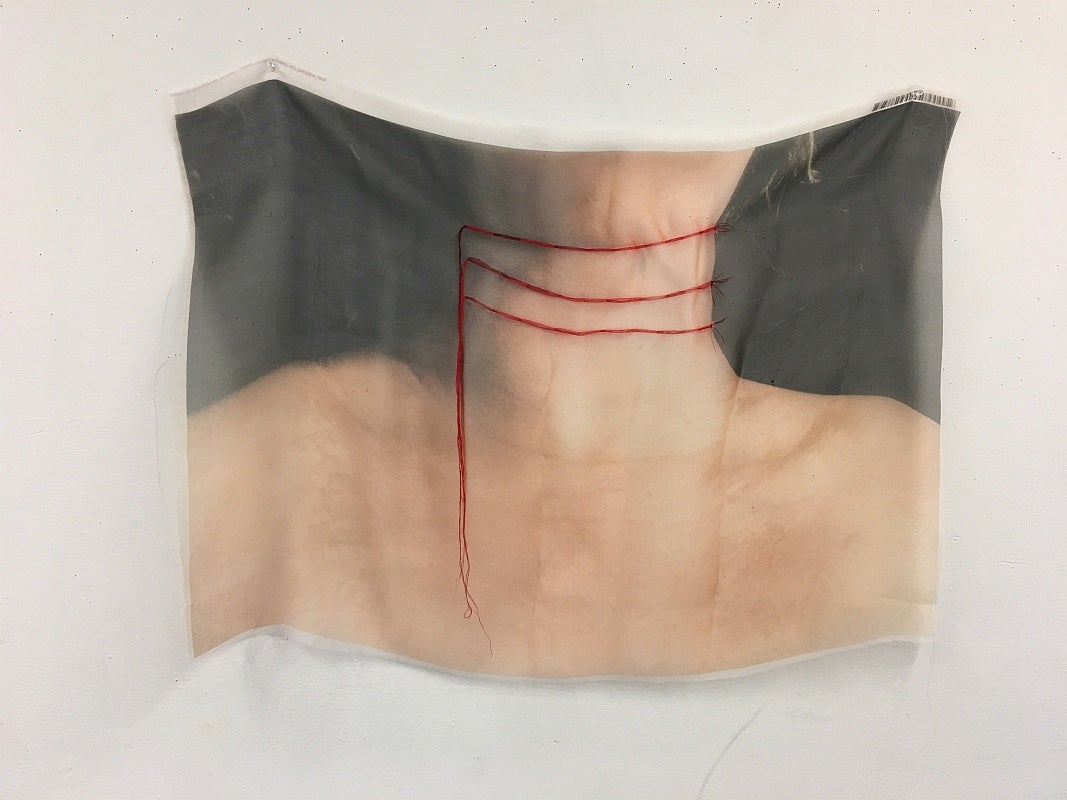 Colour photograph printed on sheer fabric depicting a person's neck and shoulders.  Red thread is embroidered in three lines across the neck with the remaining thread hanging down..