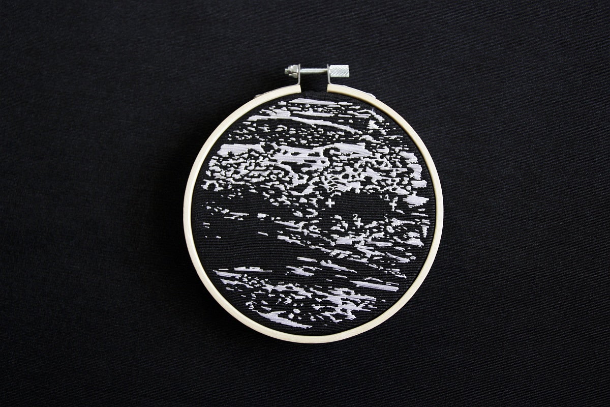 Embroidery depicting an ultrasound done in white thread on black canvas in an embroidery hoop,