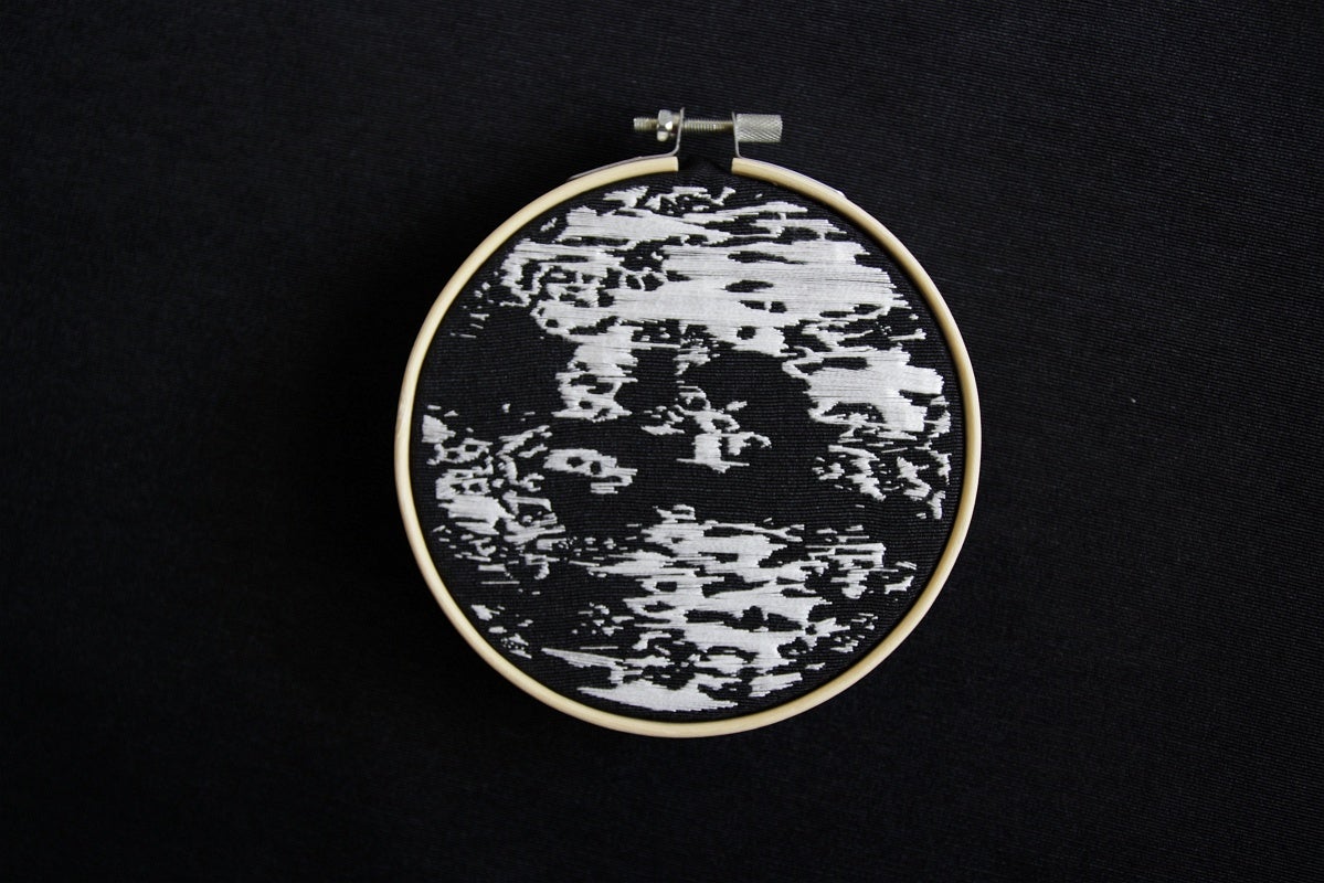 Embroidery depicting an ultrasound done in white thread on black canvas in an embroidery hoop,