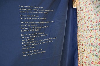 Close-up of hanging fabric with a poem embroiderd in yellow thread on dark blue fabric. 