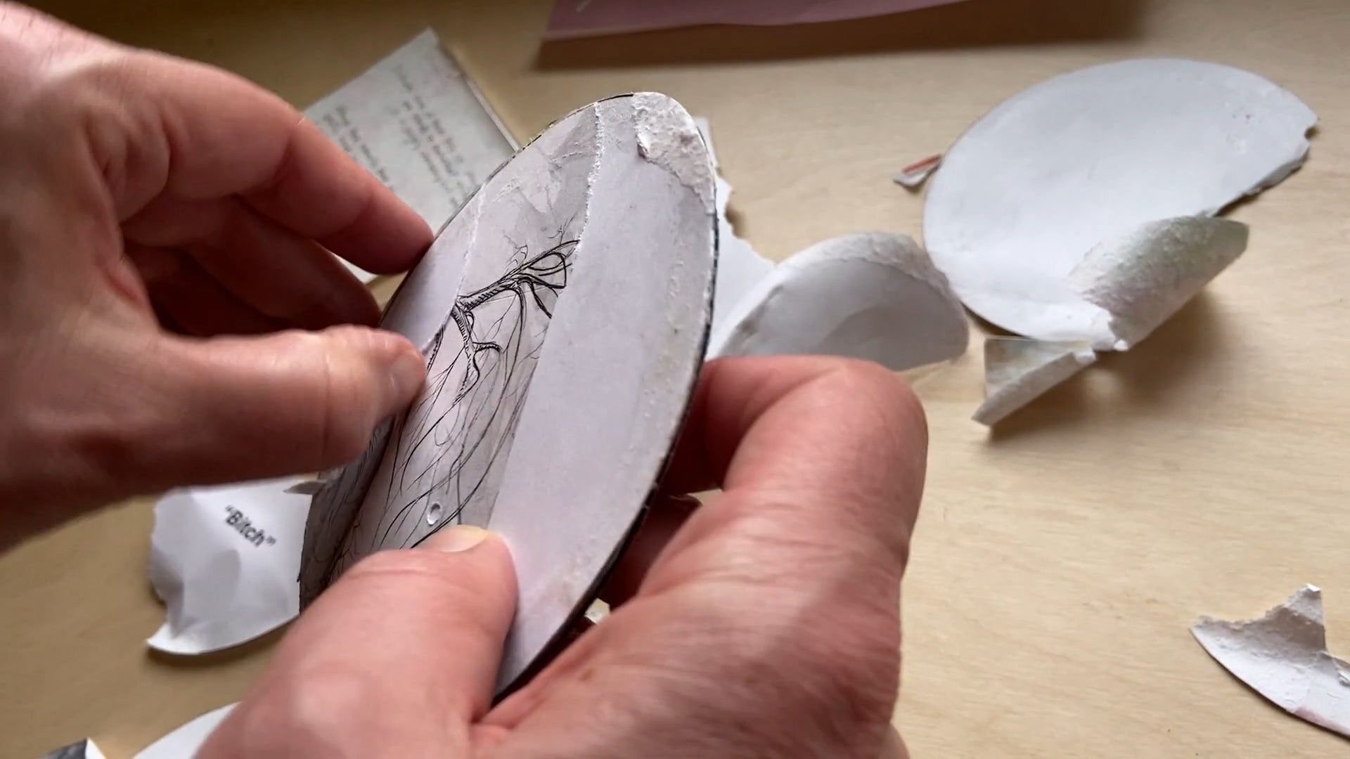 Two hands peal back paper to reveal a pen and ink drawing of a tree