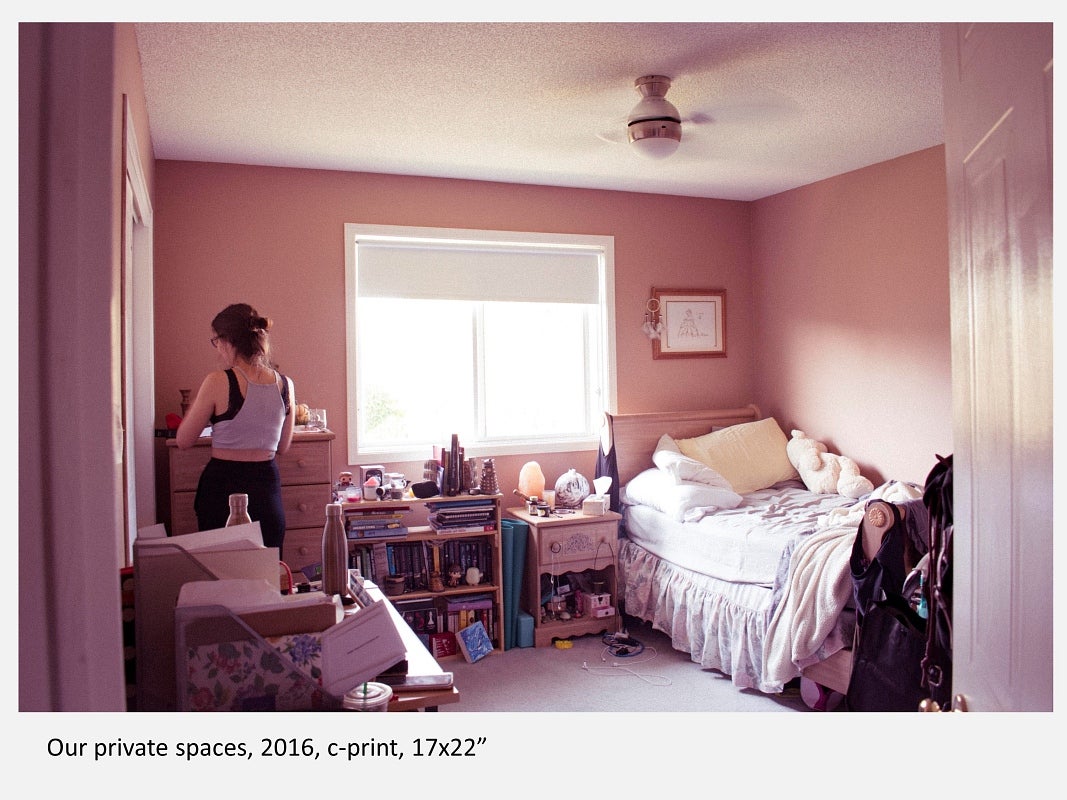 Warm-pink tinged photograph of person standing in a cluttered bedroom