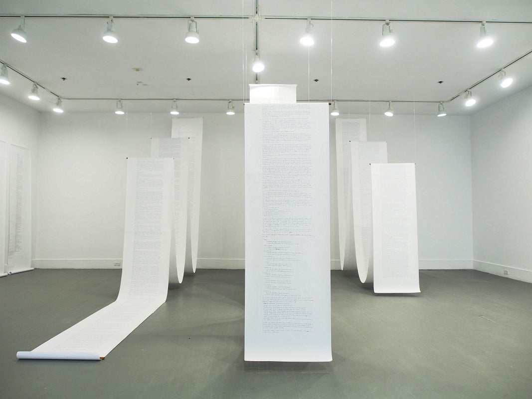 Art installation of several long rolls of paper, covered with writing, hanging from the ceiling