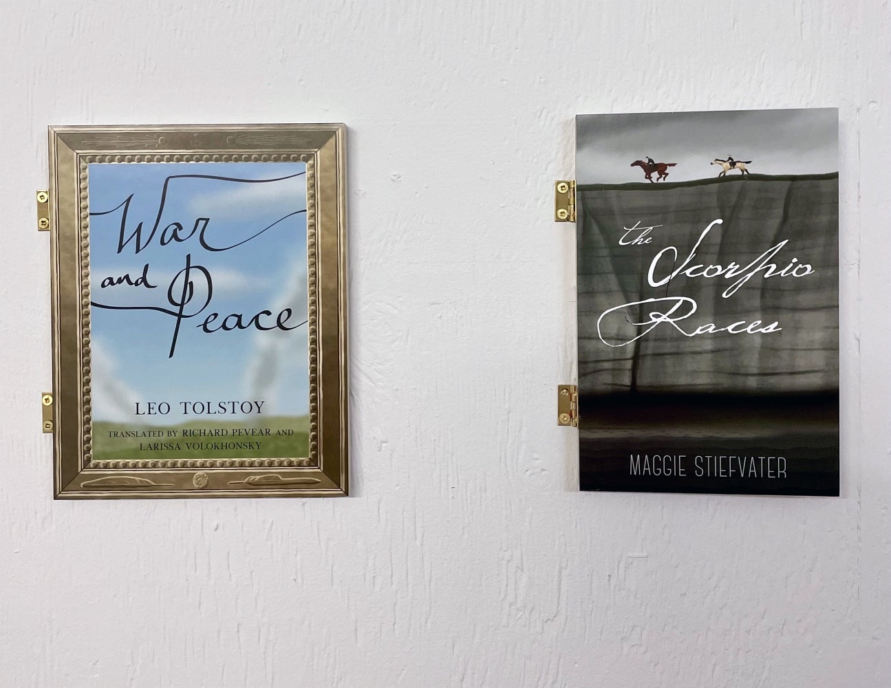 Art installation of 2 book covers attached to the wall with hinges titled "War and peace" and "The scorpio races"