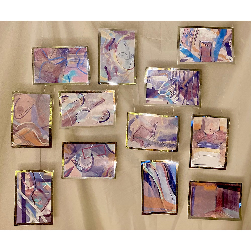 Twelve small abstract paintings in shades of mauve, blue, brown and gold hang suspended against a cloth.