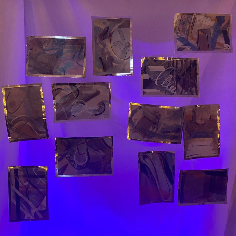 Purple and blue light on12 small abstract paintings hanging suspended.  Artworks edged with reflective material.