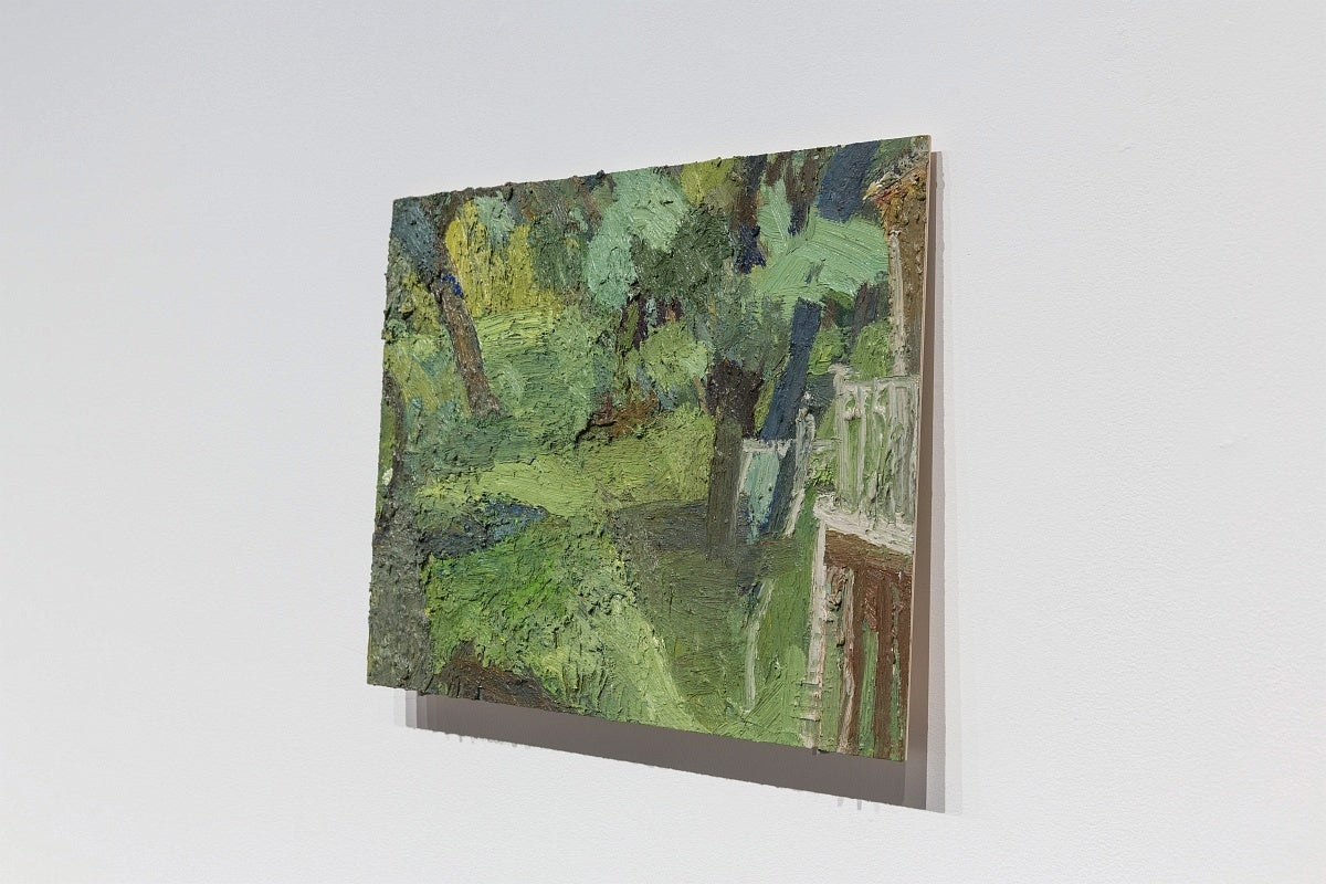 View from the side of a small, thickly painted, tropical landscape. The painting, on thin board, sits on two nails.