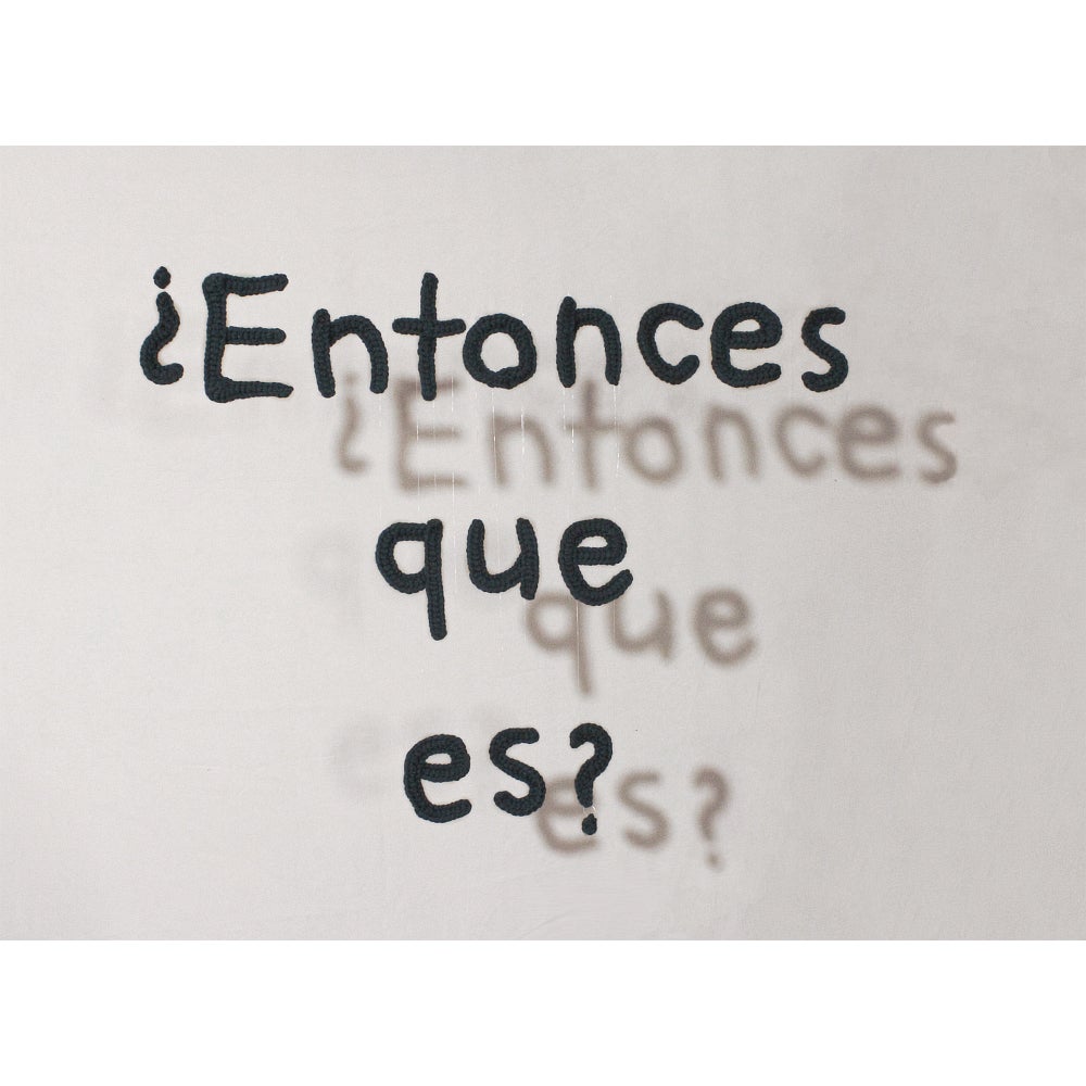 Hanging alphabetic letters cast a shadow on the wall behind.  Text reads "¿Entonces que es?"