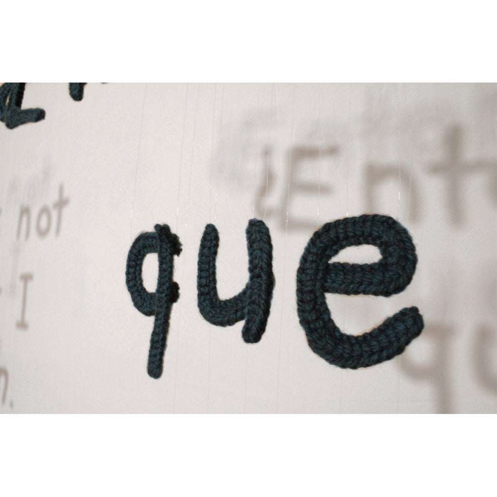 Hanging alphabetic letters cast a shadow on the wall behind.  Text reads "que"