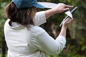 A woman wearing a blue cap carefully sharpens a scythe using a wet stone.