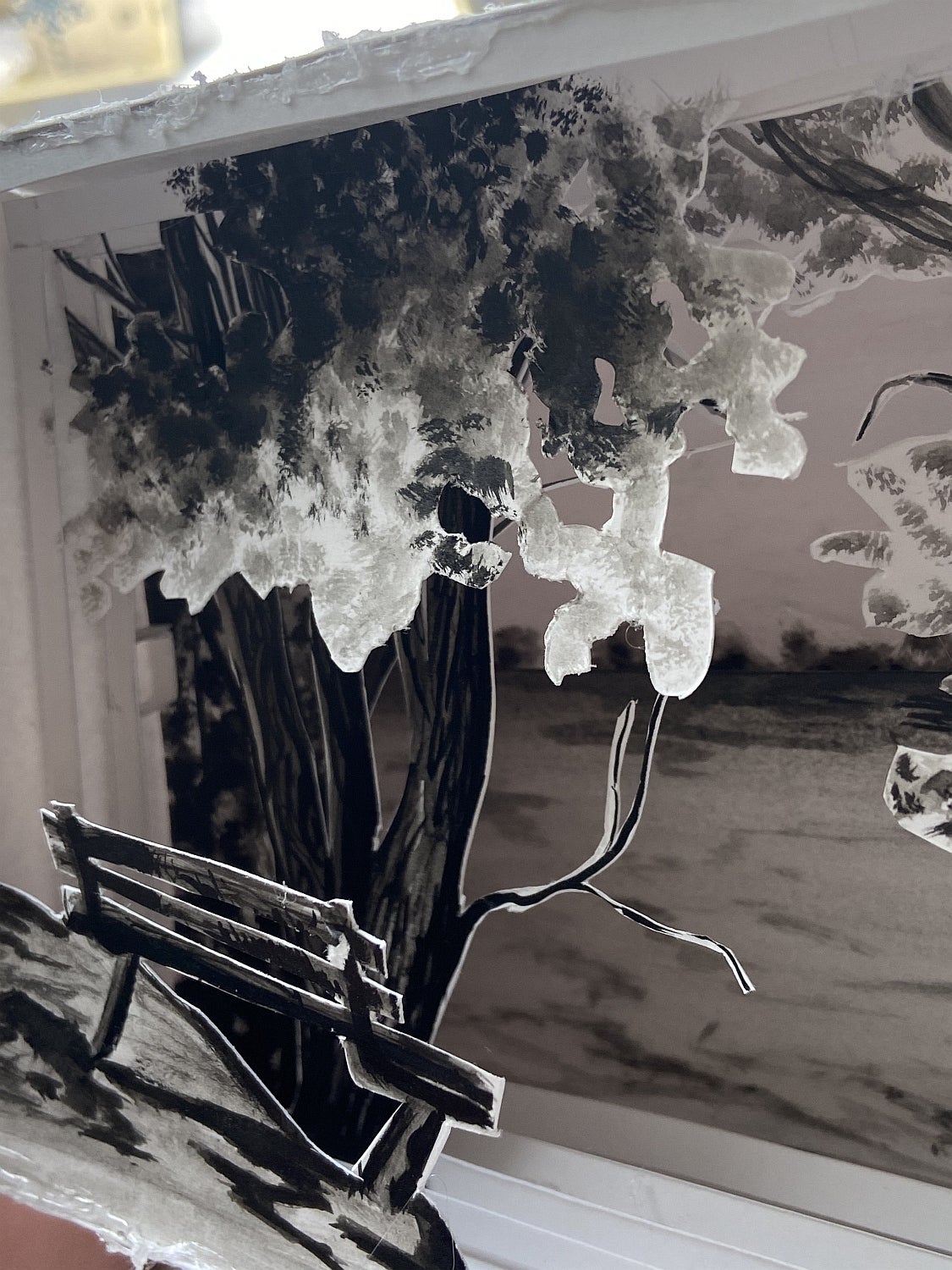 Shadow box made of paper layers showing a landscape with trees and a park bench in front.