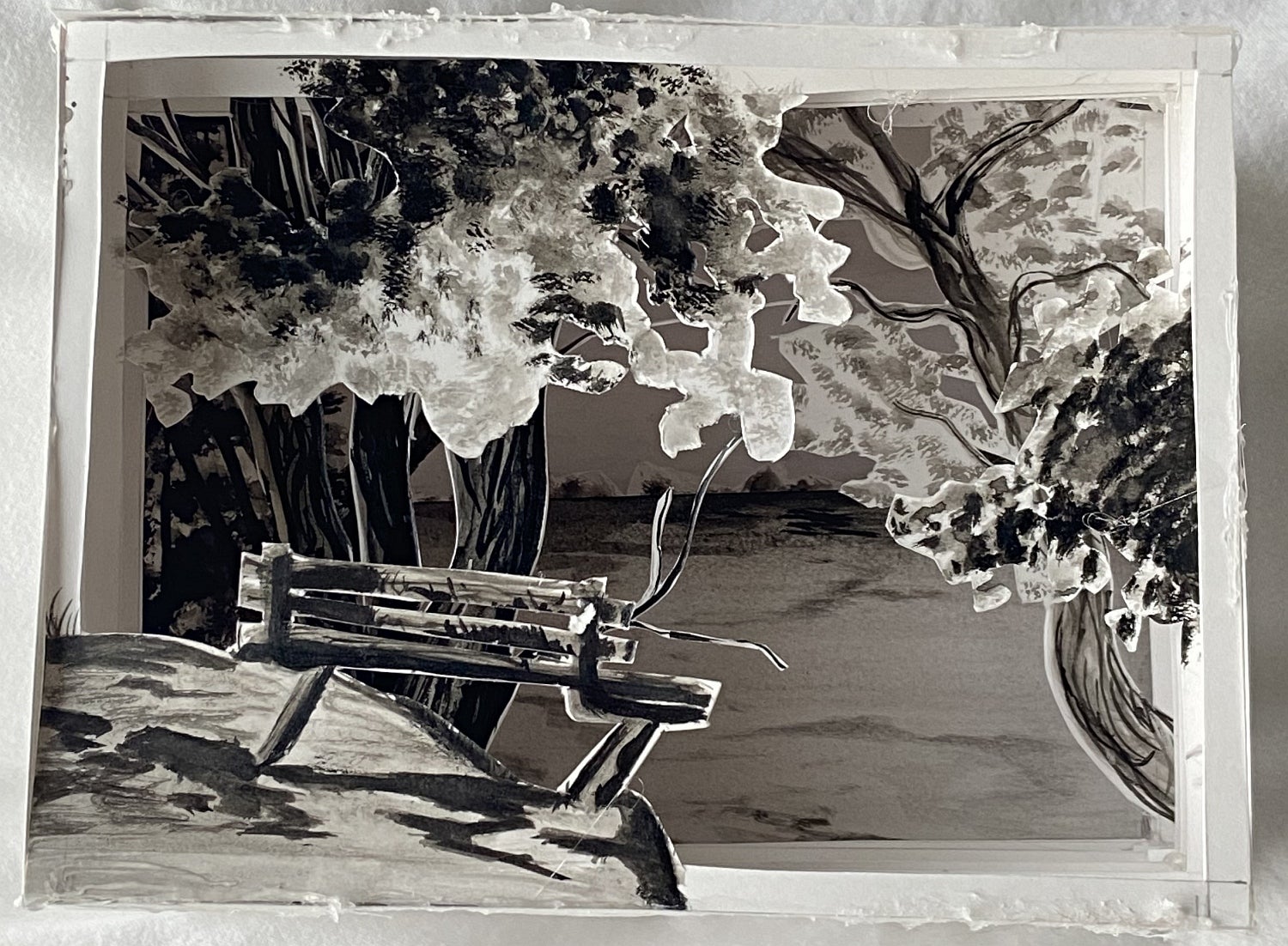 Shadow box made of paper layers showing a landscape with trees and a park bench in front.