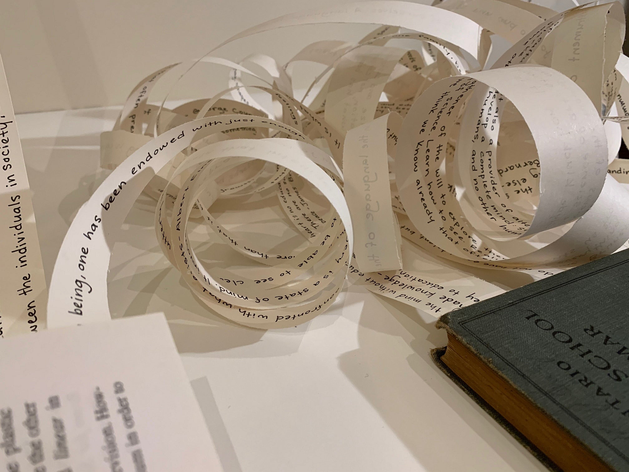 Art installation of three books lying on the floor with strips of paper coming from inside the books and stretched up the wall