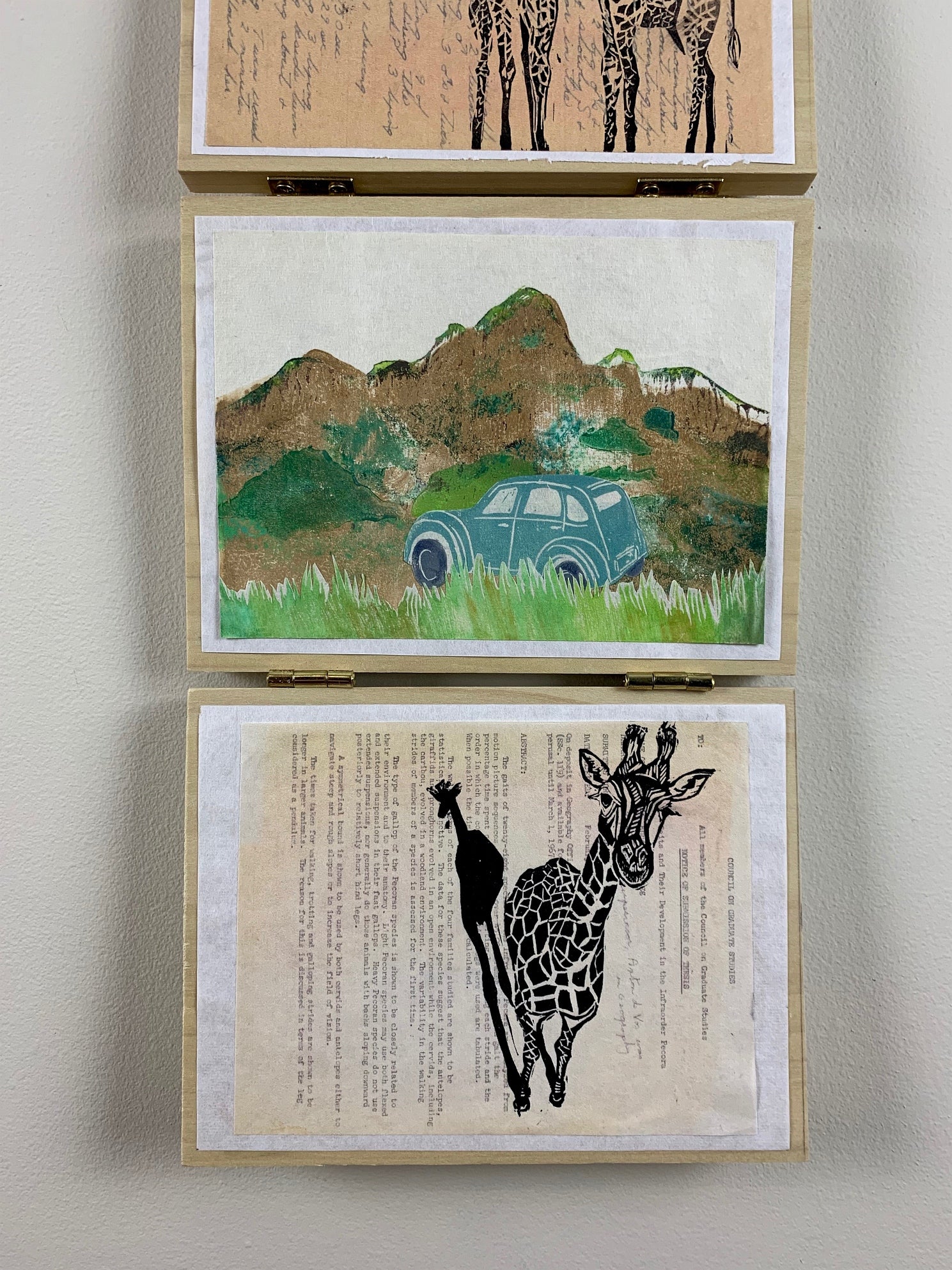 Two works of art hanging, top shows landscape is browns and green with a vintage blue car, lower two giraffes printed over text