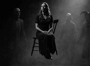 Black and white image of a woman sitting on a floating chair surrounded by fog and ghostly costumed figures.