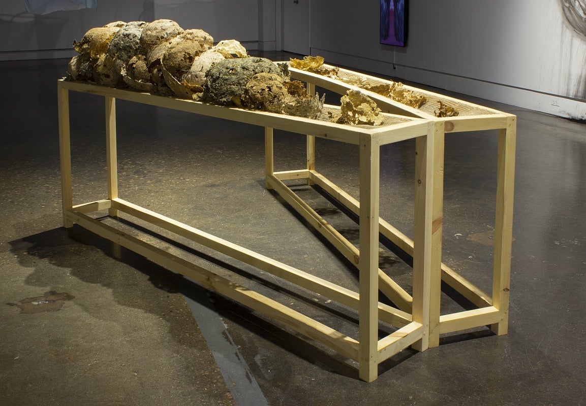 Two narrow wood tables in the holds balls of dried organic material in a darken art gallery.