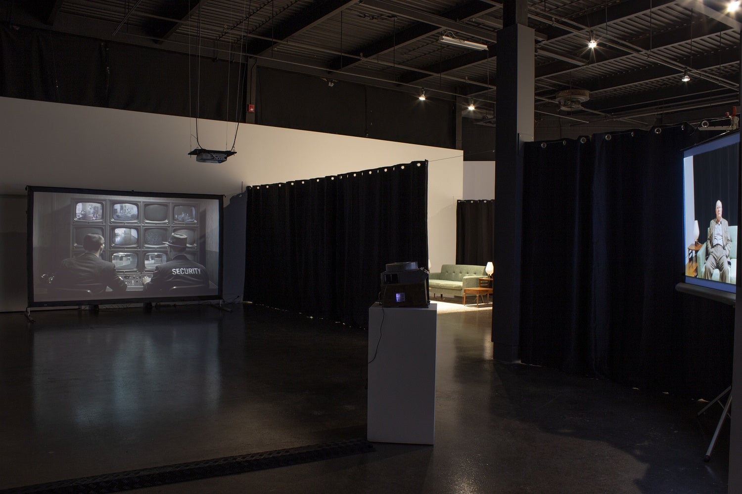 Art gallery with projections of security personnel surveilling screens and projected AI aged photos is 