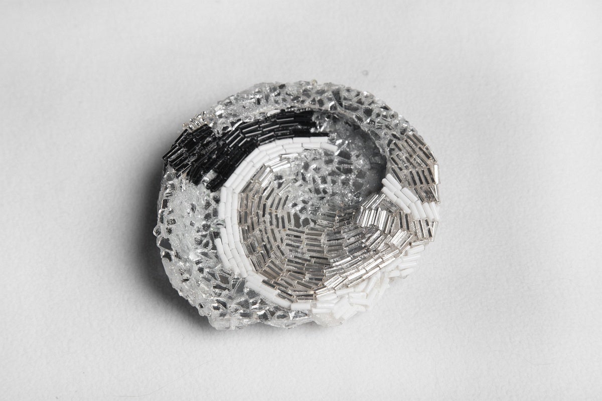 Shell-like shaped sculpture made of black, white and clear cylindrical beads and small mirrored pieces glued in a spiral pattern.