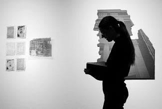 Silhouette of a person reading a book while standing in front of artwork depicting classical architecture.