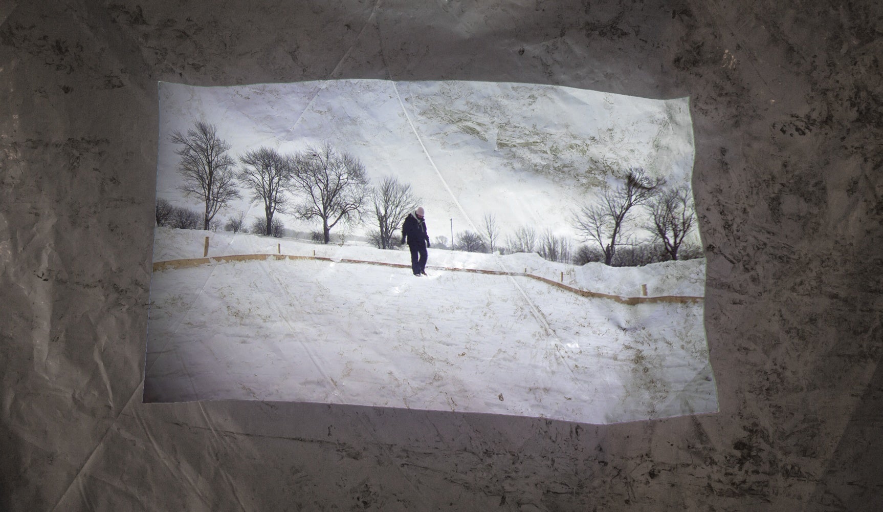 A video of a person in winter clothing tramping down snow is projected against a crumpled white tarp.