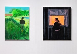 Two paintings on white wall.  On left, bright green landscape with person walking towards covered bridge. On right person in dar