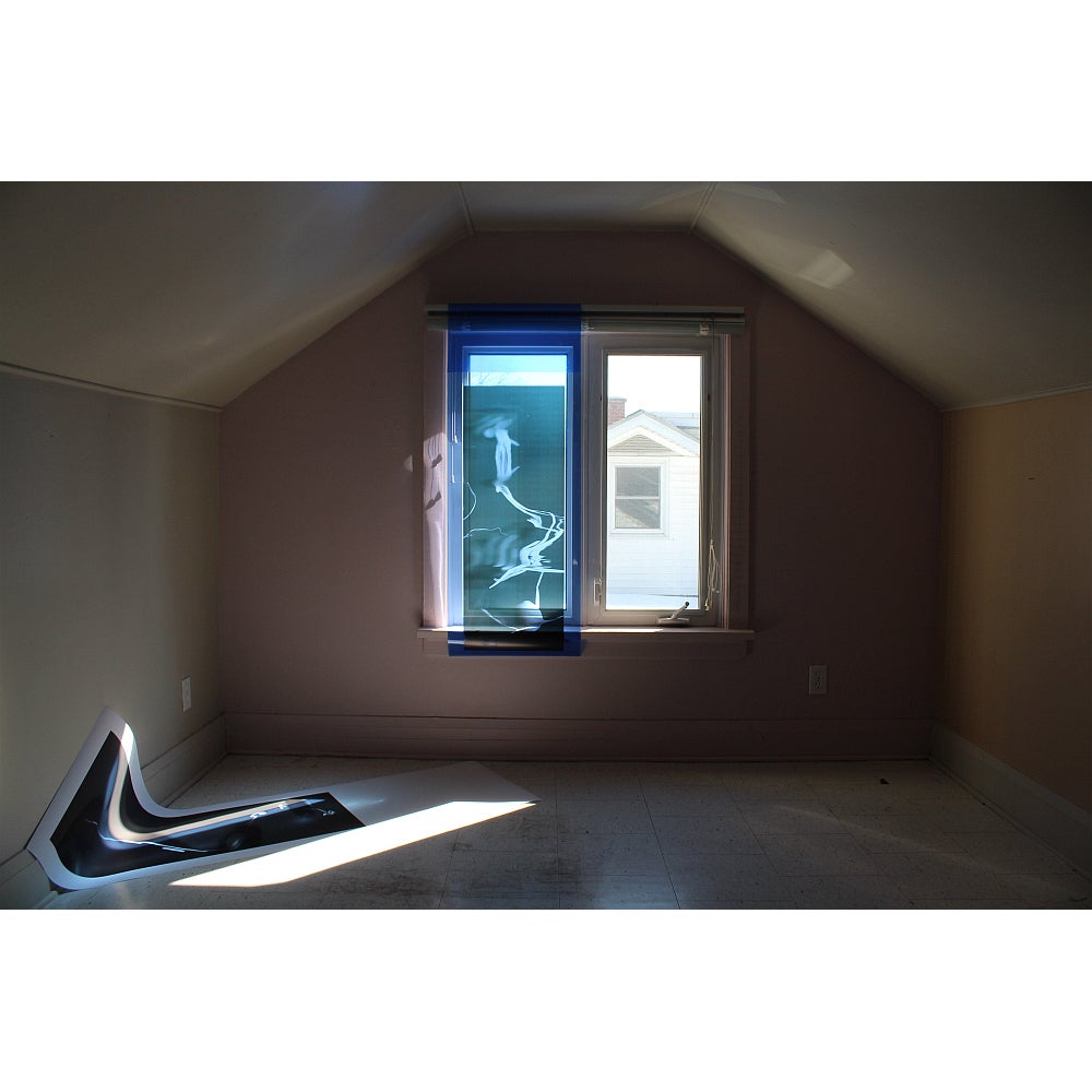 Empty room with light coming through window shining on paper picture on floor.  One window pane covered with transparent blue