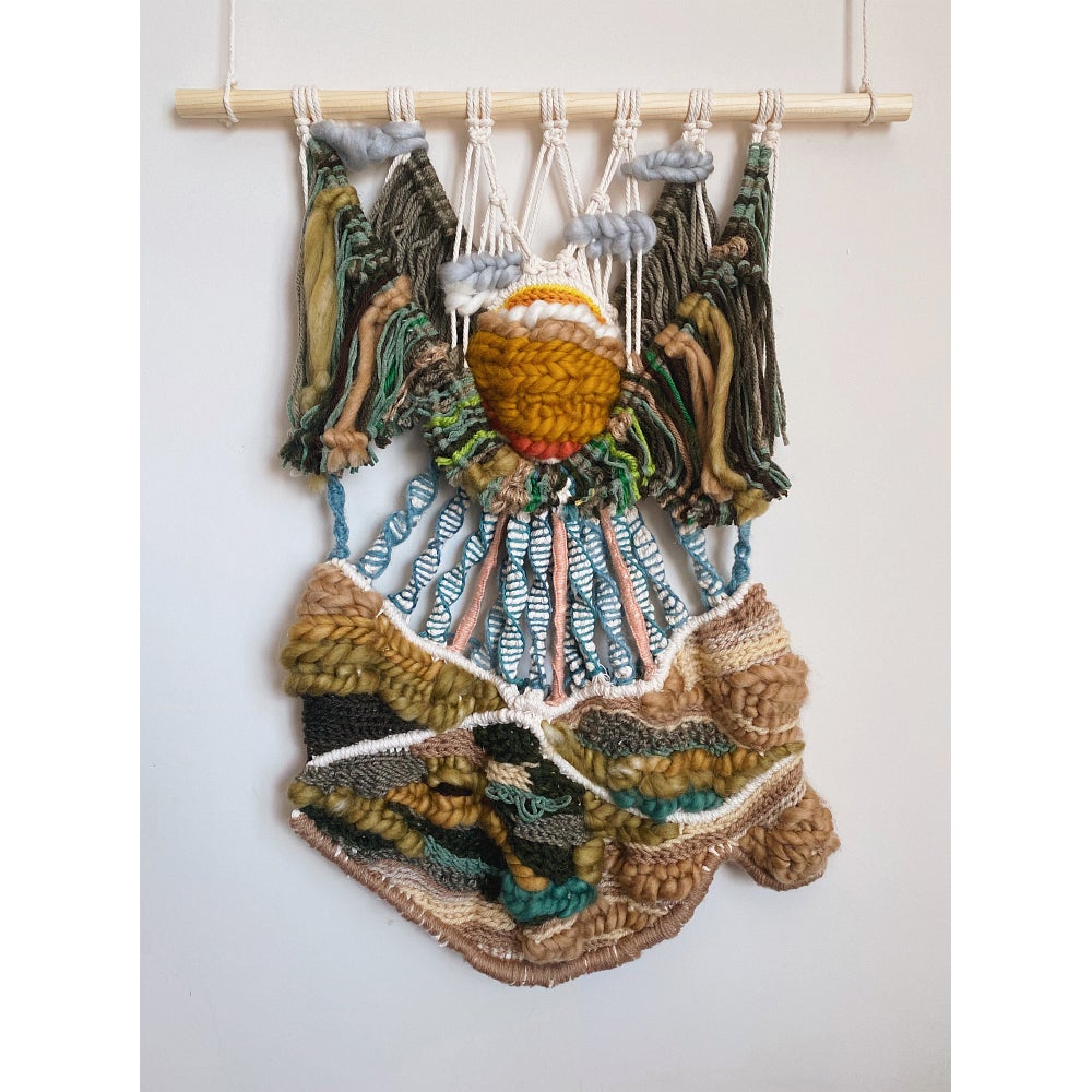 Wall hanging of patterned knotted yarn hangs from a dowel. Blue and white lines suspend an earth tone strip from a yellow circle