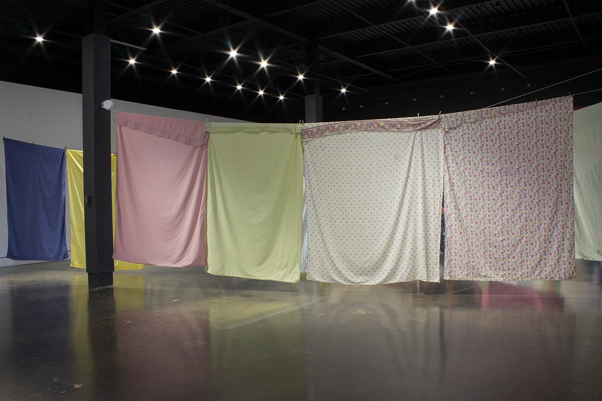 View of an art exhibition with multi-coloured and patterned bedsheets hung on what resemble clotheslines.