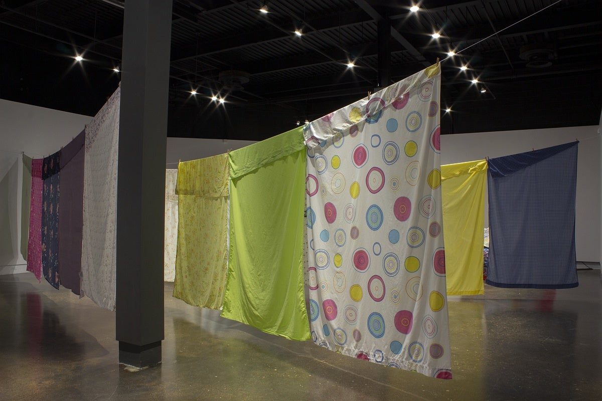 View of an art exhibition with multi-coloured and patterned bedsheets hung on what resemble clotheslines