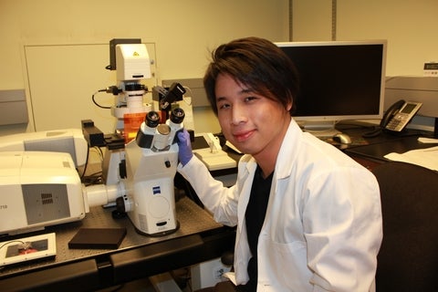 Roger Chen wearing labcoat infront of confocal microscope.
