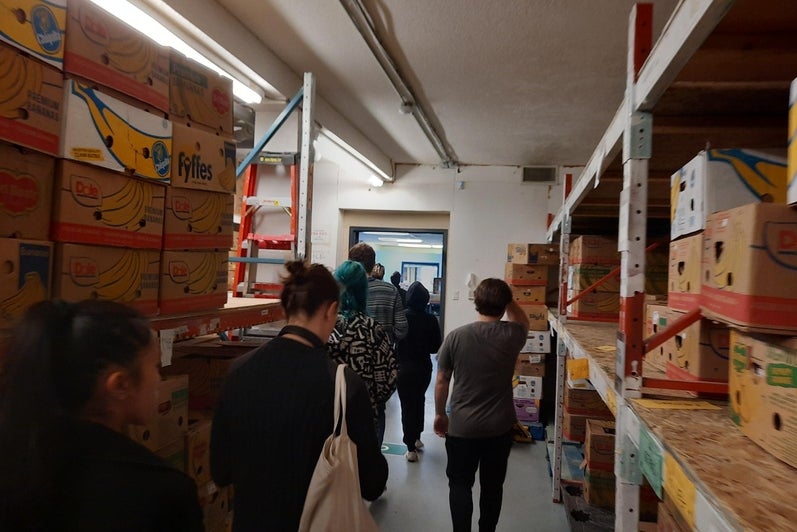 Students walking through shelves of boxed food at the Cambridge Food Bank