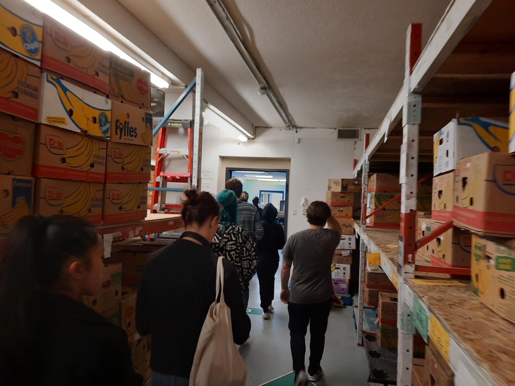 Students walking through shelves of boxed food at the Cambridge Food Bank